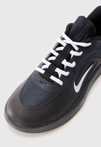 Crne atletske tenisice s mrežastim gornjim dijelom, podstavljenim jezikom, bijelim vezicama i glatkim gumenenim đonom sa naglašenim logom sa strane.