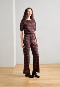 Bordeaux gemustertes Zweiteiler-Outfit mit einem kurzärmeligen Top und weiten Hosen, das ein strukturiertes Design und schwarze Ankle Boots aufweist.