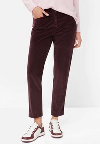 Bordeauxfarbene Cordhosen in Slim Fit, mit einer vorderen Tasche und einer glatten Textur. Kombiniert mit weißen und bordeauxfarbenen Sneakers.
