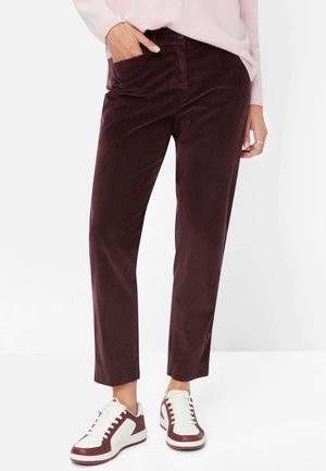 Bordeauxfarbene Cordhosen in Slim Fit, mit einer vorderen Tasche und einer glatten Textur. Kombiniert mit weißen und bordeauxfarbenen Sneakers.