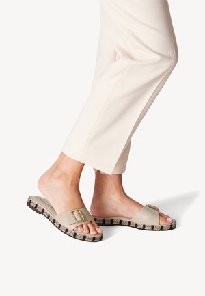 Beige slide sandals with a large buckle, woven jute-like sole, and a textured black-and-white pattern along the edge.