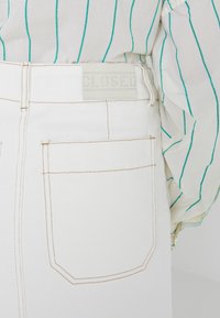 Witte denim jeans met een achterpatch met "CLOSED" in reliëf. Gedetailleerde stiksels en een enkele achterzak zijn zichtbaar.