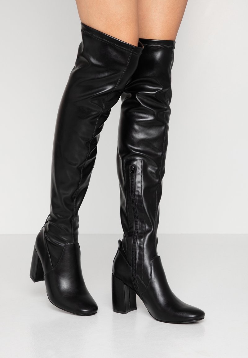 Botas negras hasta la rodilla, hechas de cuero suave, con puntera afilada y tacón cuadrado. Presentan un cierre lateral y un diseño ajustado y elegante.