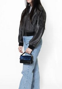 Giubbotto bomber in pelle nera con polsini a coste, abbinato a jeans a vita alta di colore blu chiaro e una piccola borsa con un design a strisce zebra blu.