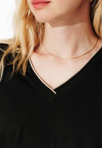 Haut noir à col en V avec un contraste de bord clair, fabriqué en tissu doux. Design ajusté, présentant une texture subtile au niveau de l'encolure.