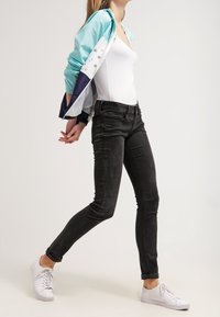 Czarne obcisłe jeansy z teksturowanym wykończeniem, zestawione z jasnoniebieską i granatową kurtką przeciwwiatrową. Całość dopełniają białe trampki.