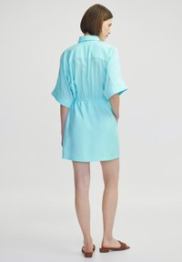 Robe chemise bleu clair avec des manches courtes, taille cintrée et un col. Tissu lisse et léger avec un design décontracté.