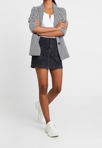 Černobílý houndstooth blazer, bílý top, tmavá džínová sukně a bílé tenisky. Hladké textury a dobře střižený design s přiléhavým siluetou.