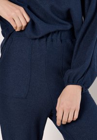 Navyblaues, strukturiertes Strick-Loungewear-Set mit elastischem Bund. Lange, puffärmel und seitliche Taschen an den Hosen. Weicher, lässiger Schnitt.