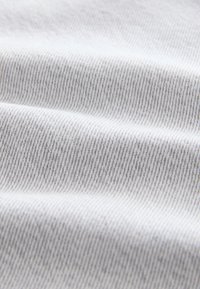 Primo piano di tessuto bianco con sottili linee diagonali grigie e pieghe morbide che creano una superficie testurizzata.