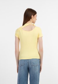 Gul ribben T-shirt med korte ærmer, der har en åben rygudskæring. Sammen med løstsiddende blå denim jeans.