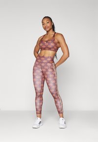 Sport-BH og tights-sett i brunt med oransje blomstermønster. Tightsene har sidestiper og høy midje. Hvite treningssko.