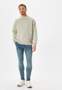 Felpa grigia chiaro con maniche a raglan, abbinata a jeans azzurri aderenti e sneakers bianche con accenti marroni. Completo semplice e casual.