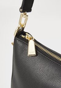 Black textured leather handbag with gold hardware, featuring a zip closure and a detachable strap. Notable gold zipper pull detail.