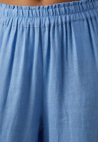 Tissu bleu clair, texturé, d'un pantalon ample avec une taille élastique et de douces plis pour le confort et la liberté de mouvement.