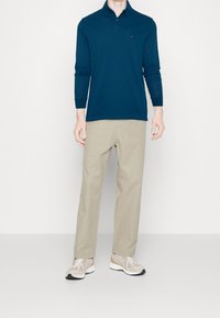 Mörkblå långärmad polo med krage, kombinerad med ljusbeiga byxor och beige sneakers med vita accenter. Enkel och avslappnad design.