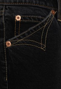 Musta farkkutakki, jossa on kontrastivärinen kultainen tikkaus, kuparinapin, ja ainutlaatuinen taskusuunnittelu, jossa on kärjellinen muoto. Raikas kangas.