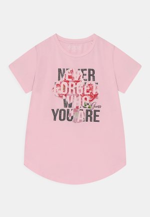 Jasnoróżowa koszula z krótkim rękawem z kwiatowym wzorem krzyża i napisem "Nigdy nie zapominaj, kim jesteś" czarnymi i różowymi literami.