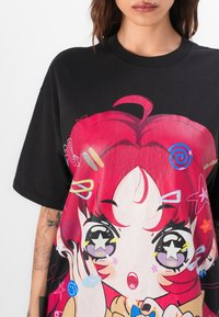 Black oversized t-shirt featuring a colorful graphic of a surprised character with red hair, stars, and various playful accents.