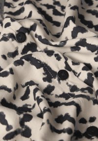 Tessuto di cotone con stampa leopardata beige e nera, caratterizzato da bottoni neri e una superficie morbida e testurizzata, che mette in mostra pieghe e grinze.