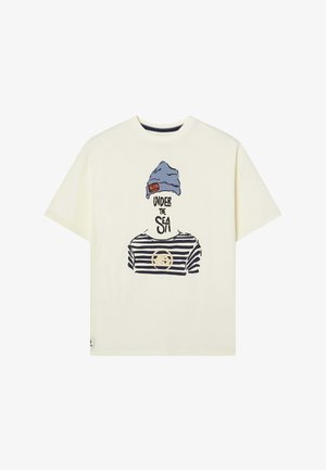 Camiseta crema con un gráfico de una persona con un gorro azul y una camisa de rayas horizontales con el texto "BAJO EL MAR". Manga corta.
