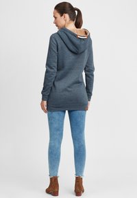 Felpa blu scuro con fodera texturizzata beige, maniche lunghe e tasche laterali. Abbinata a jeans skinny azzurri e stivali alla caviglia marroni.