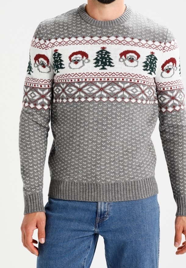 Homme portant un pull de Noël gris orné de visages du Père Noël et de motifs de sapins, assorti à un jean bleu.