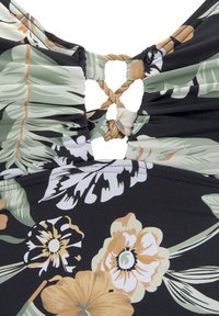 Maillot de bain noir en tissu avec un motif floral en vert, jaune et blanc, et un détail noué à l'arrière.