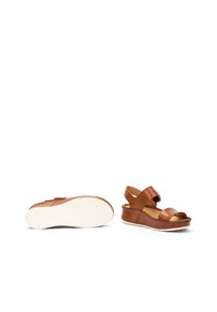 Sandalias de cuero marrón con diseño de cuña, que presentan dos correas anchas, punta abierta, detalle de borde trenzado y una suela blanca texturizada.