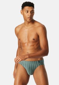 Herrenschwimmbrieftaschen in gedämpften Teal mit vertikalen Streifen, verfügen über ein enganliegendes Design und einen einfachen Bundakzent. Das Material scheint glatt und elastisch zu sein.