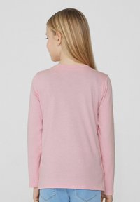 Růžové tričko s dlouhým rukávem vyrobené z měkké bavlny, s jednoduchým kulatým výstřihem a rovním lemem, nošené s světle modrými džíny.