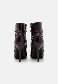 Brune lærhøye ankelstøvler med glidelås, med kryssremmer og en elegant, jevn tekstur.