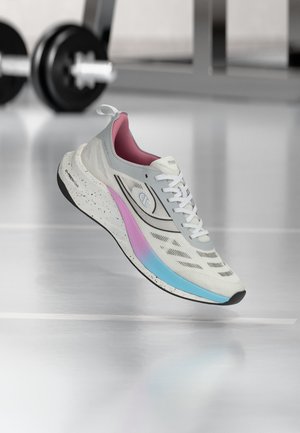 Chaussure de course blanche avec des accents de semelle rose et bleue flottant près du sol de la salle de sport, barres de musculation noires floues en arrière-plan.