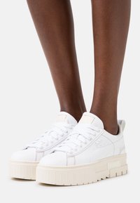 Vita plattformssneakers med en slät läderöverkappa, rund tå och vita snören. Har subtil beige sömnad och varumärke på sidan.