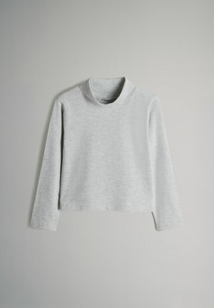 Šviesiai pilka ilgos rankovės trumpa turtleneck marškinėliai su minkšta, lygiška medžiaga, kabančia prieš paprastą foną.