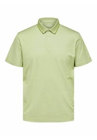 Polo de color verde claro hecho de tela suave, con cuello clásico, tapeta de tres botones y mangas cortas. Diseño sencillo, sin patrones.