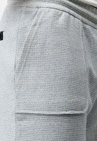 Shorts de sport bleu clair fabriqués en tissu texturé, avec une poche latérale et une taille élastique pour le confort et l'ajustement.