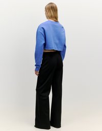 Gekürzter blauer Sweatshirt mit langen Ärmeln, kombiniert mit schwarzen weit geschnittenen Hosen. Der Stoff wirkt weich, und beide Kleidungsstücke haben eine lockere Passform.