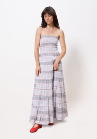 Trägerloses Maxikleid in einem blau-rosa karierten Muster mit gestuften Rüschen am Saum. Getragen mit roten Ballerinas.