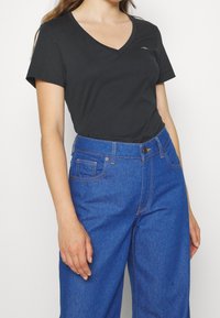 Černé tričko s výstřihem do V vyrobené z bavlny, spárované s modrými džínami s vysokým pasem. Tričko má krátké rukávy a přiléhavý střih.