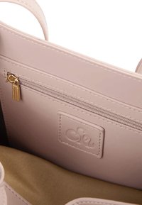 Jasnoróżowa torebka z zamkiem błyskawicznym, złotymi akcentami, gładką skórzaną teksturą oraz naszywką z logo wewnątrz.