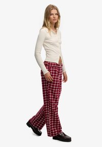 Kremowy prążkowany top z długim rękawem i falowanym dołem, zestawiony z czerwonymi szerokimi spodniami w kratę. Całość dopełniają czarne loafersy.