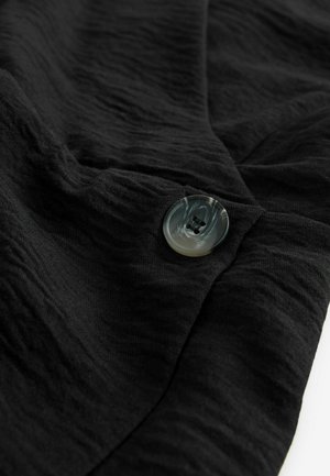 Sort stof med en tekstureret overflade og en rund, marmoragtig knap med to huller. Stoffet er draperet og en smule foldet.