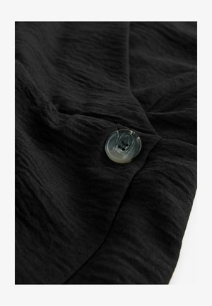 Melna auduma ar teksturētu virsmu un apaļu, marmora līdzīgu pogu ar divām caurumiem. Audums ir sakrauts un nedaudz krunkains.