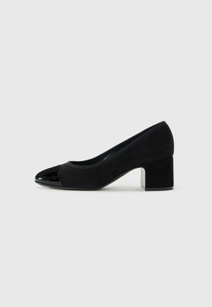 Chaussure à talon bas en daim noir avec un bout brillant noir, vue de côté sur un fond gris clair uni.