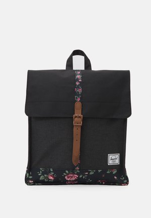 Sac à dos noir avec des accents en tissu floral, sangle marron avec boucle, poignée supérieure et un patch de marque rectangulaire blanc en bas à droite à l'avant.