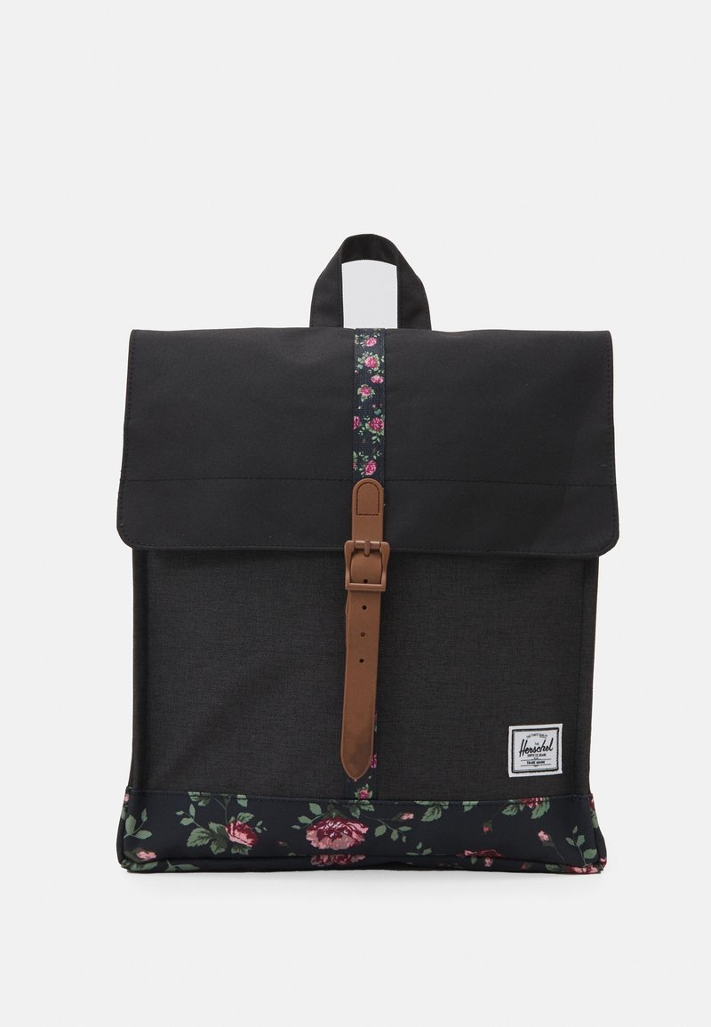 Sac à dos noir avec des accents en tissu floral, sangle marron avec boucle, poignée supérieure et un patch de marque rectangulaire blanc en bas à droite à l'avant.