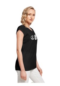Schwarzes T-Shirt mit V-Ausschnitt, kurzen umgeschlagenen Ärmeln, das zwei weiße Frieden Zeichensymbole auf der Vorderseite zeigt. Glatte Textur, lässige Passform.