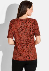 Red and black animal print top with short sleeves, round neckline, and loose fit. Textured fabric with a bold, swirling pattern.