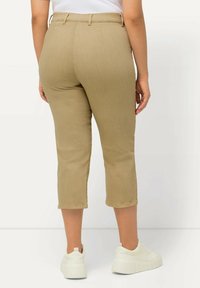 Pantalones crops color caqui hechos de tela suave con un corte ajustado, que presentan una cinturilla y bolsillos traseros, combinados con zapatillas blancas.